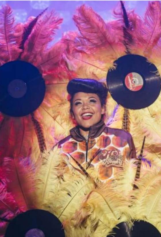 Hot Brown Honey on stage at a Fringe venue surrounded by large feathers and records made to look like flowers. Image by: David Monteith Hodge